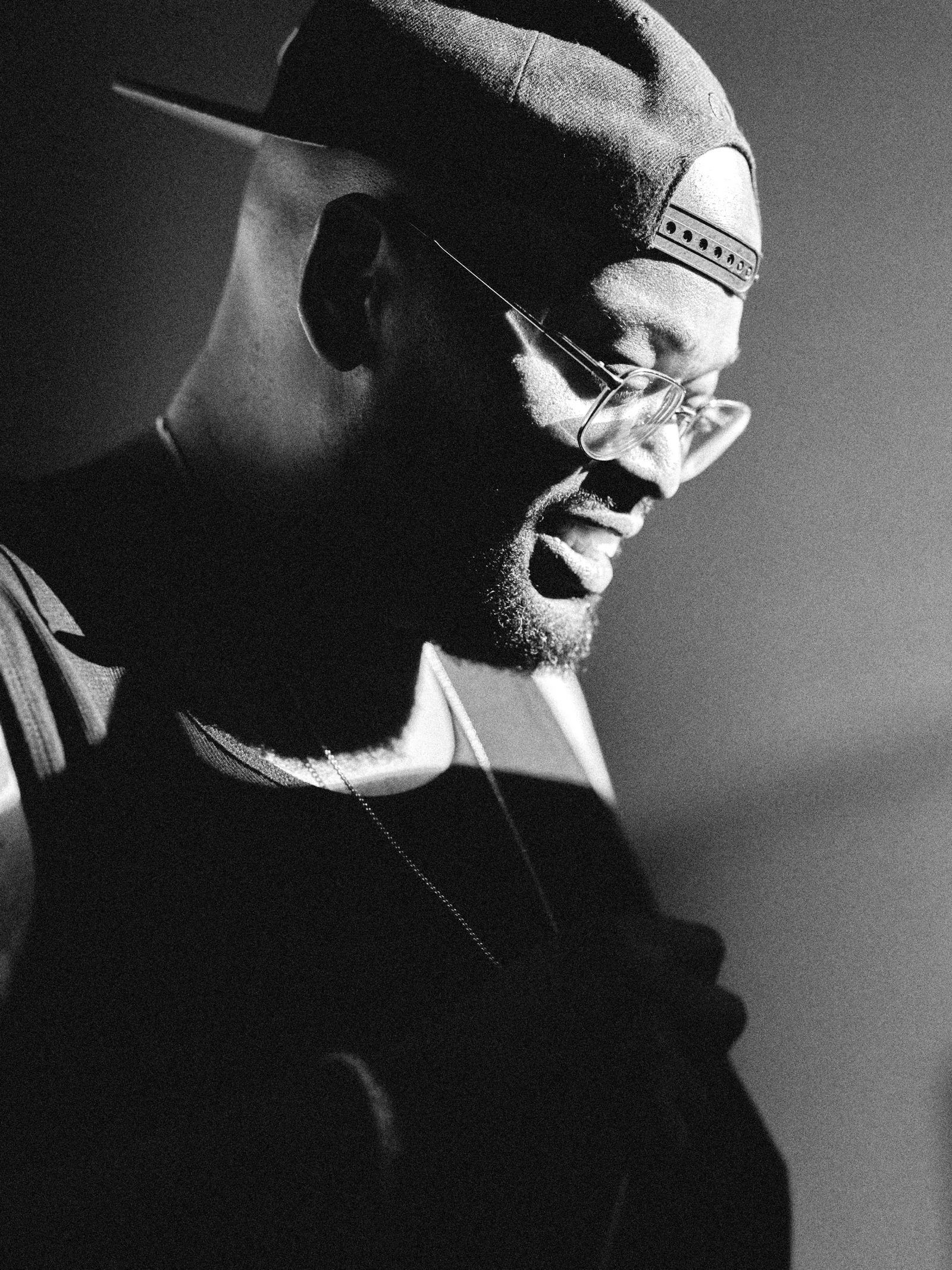 Portrait de profil d'un participant à casquette et lunettes, lumière contrastée, noir et blanc